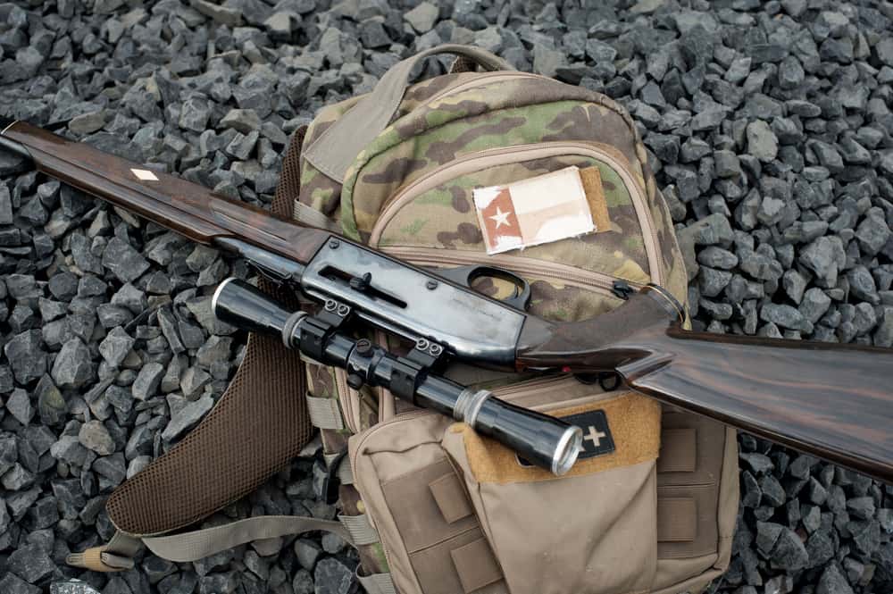 A camouflage backpack and a rifle laid on pebbles