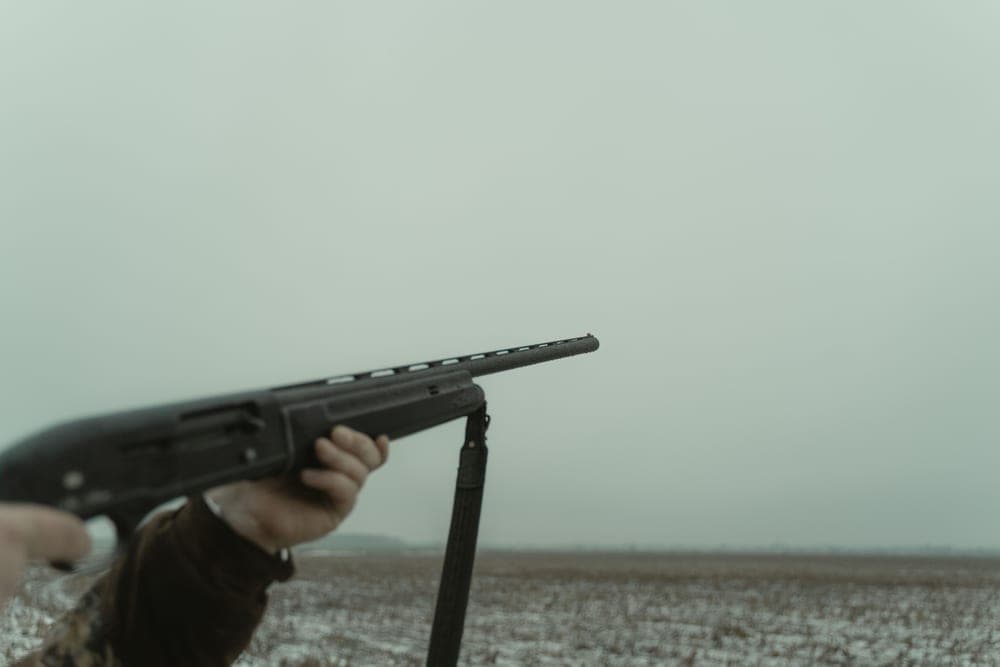 A person aiming a rifle across open countryside