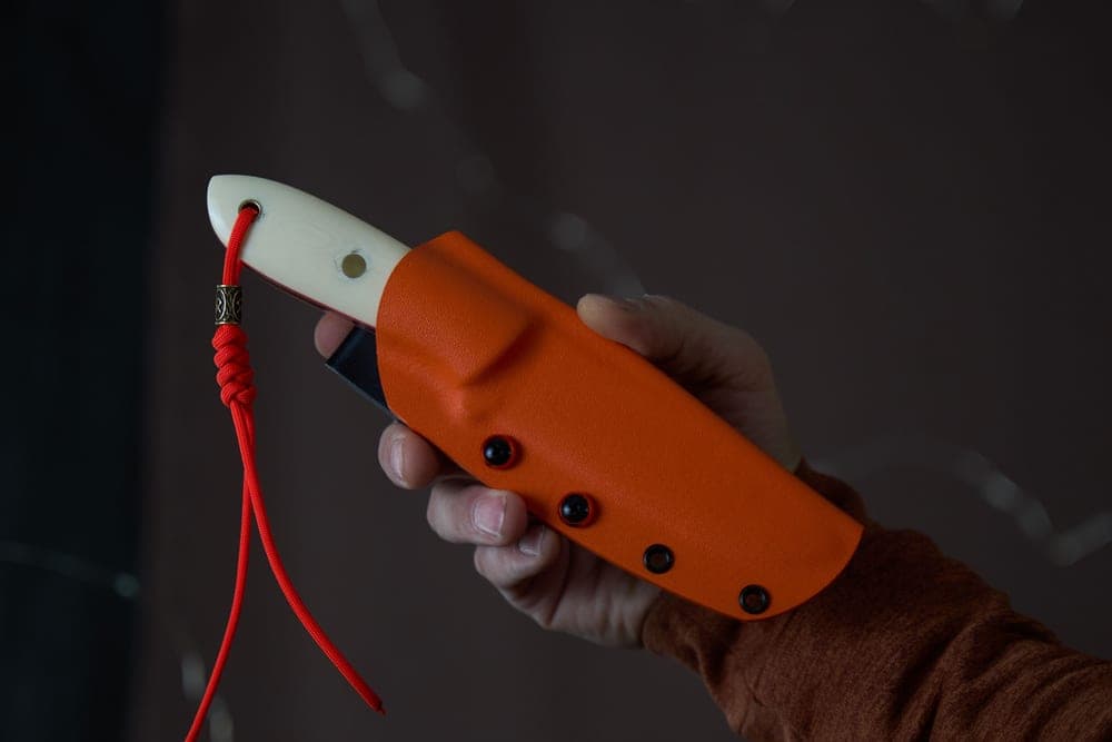 A hand holding a knife with an orange sheath