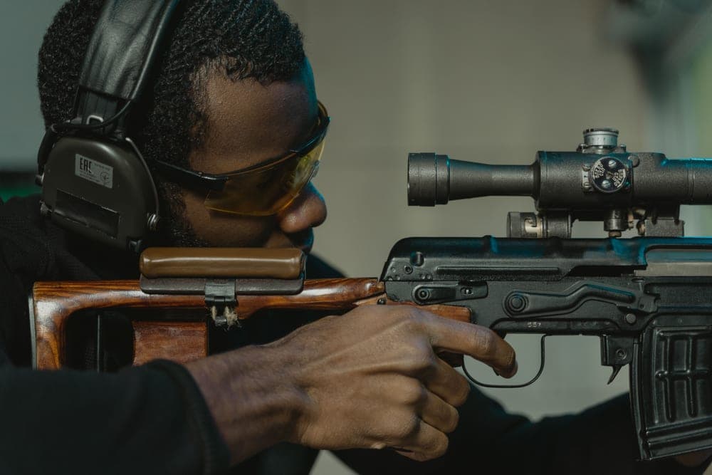 A man in eye and ear protection aiming a rifle at a shooting range